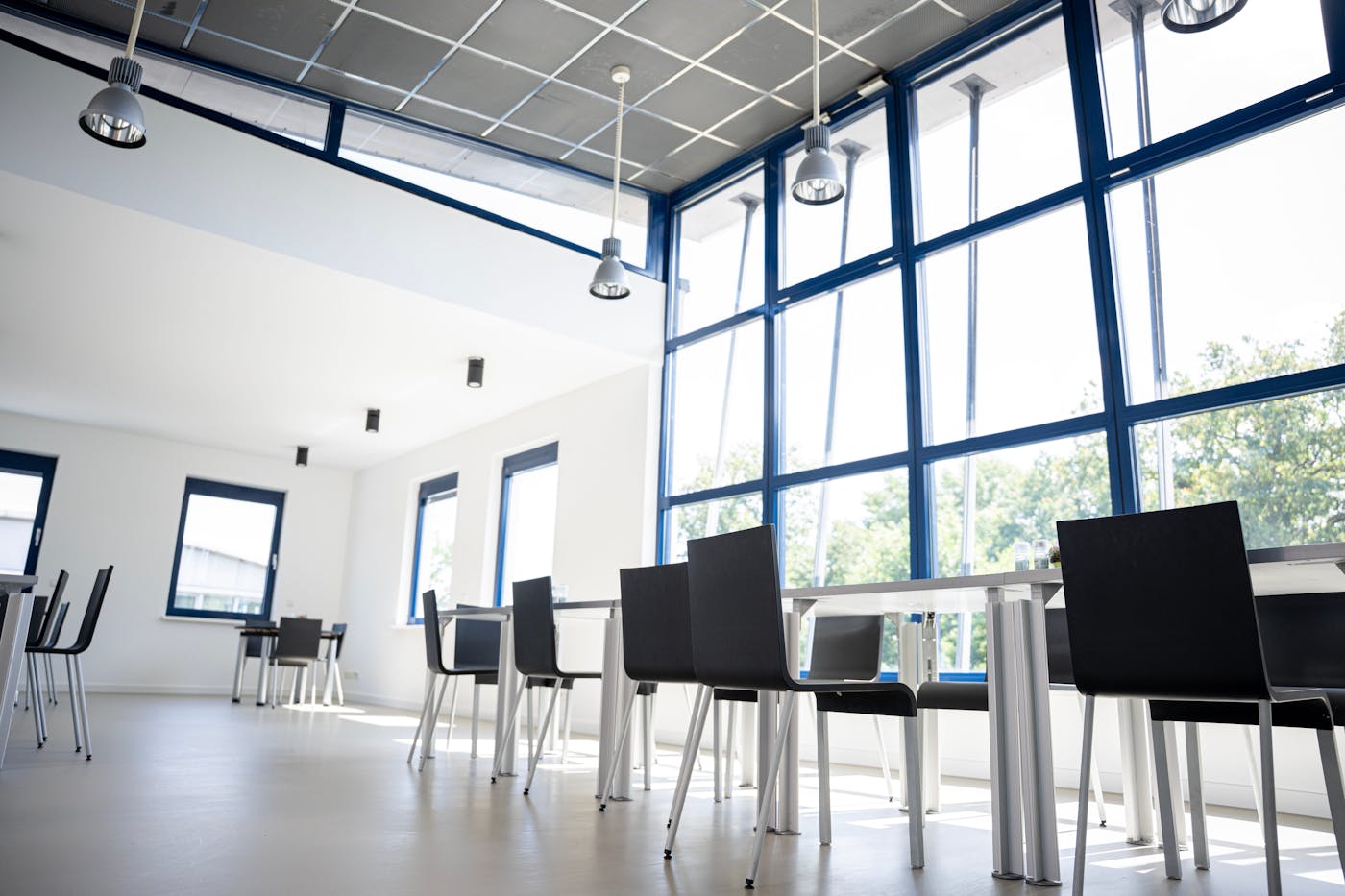 Moderne Kantine mit blau gerahmten Fenstern und weissen Tischen