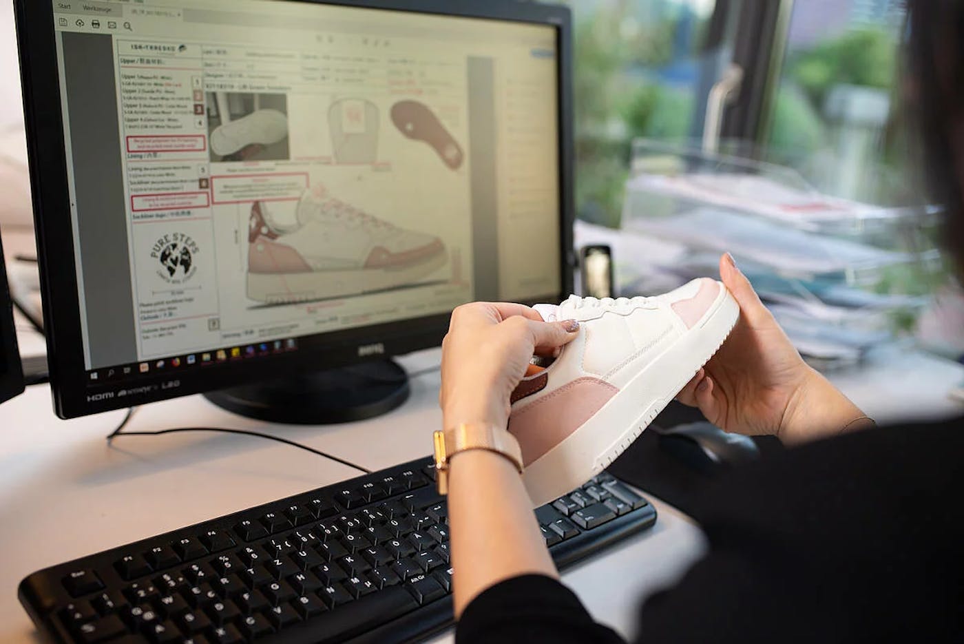 Hände halten einen Sneaker vor einem Bildschirm mit Designzeichnungen